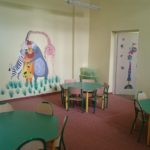 Zdjęcie przedstawiające kącik dla dzieci z nowymi stolikami, regałami, wykładziną i pomalowanymi ścianami z ozdobami na filii nr 14 z innego ujęcia